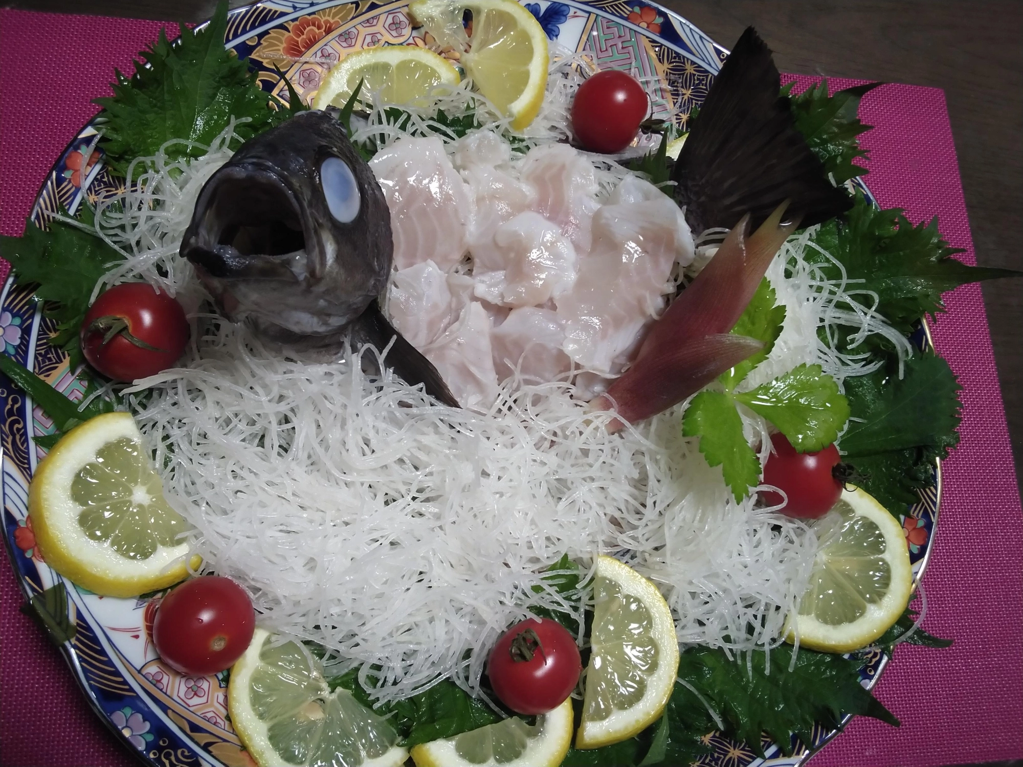 堤防のデッカイメバルの姿造り。『材料::メバル1匹、大根のツマ、檸檬、ミニトマト、大葉、茗荷』まずはメバルを頭と尻尾、むなびれを残して姿造り用に捌きます。メバルも各ヒレに鋭いトゲがありますのでハサミでカットしてから捌きます。尾頭付きの骨を酢で殺菌します。(酢締めしたら目の色が白くなっちゃいました!)大根の先っちょで台座を作って頭と尻尾を固定します。次に皿を野菜類で飾りましょう。最後に刺身を盛り付け写真写りのよい角度に修正(笑)して完成!とっても脂がのっていてすごい美味しかったです。